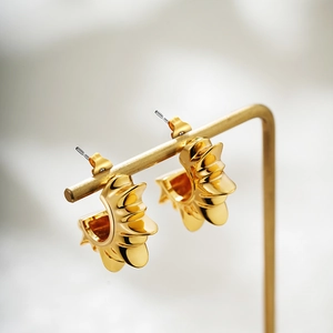 Macro shot of gold sunburst C-shaped earrings with layered abstract design on metal stand
