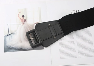 Detail of a black elastic wide waist belt featuring a large square buckle and studs