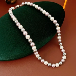 Macro view of multi-color pearl necklace with silver clasp on green velvet display