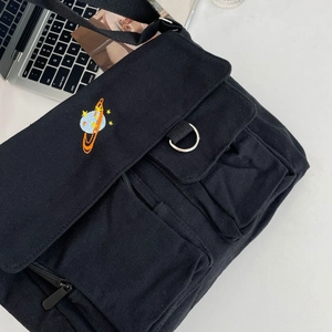 Detail of black canvas messenger bag featuring Saturn embroidery and utility pockets