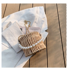 Close-up of woven straw basket bag featuring white pearl handle and metal chain detail