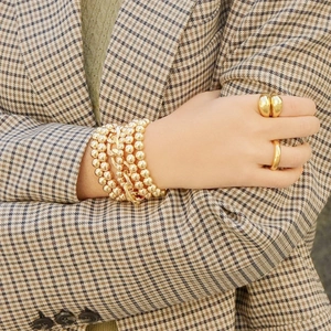 Detail view of a model wearing a gold beaded bracelet and minimalist rings with a plaid suit