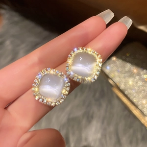 Macro shot of gold-plated square cat eye stone earrings with shimmering diamond halo