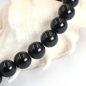 Close-up of polished black agate round beads arranged on a white natural shell background