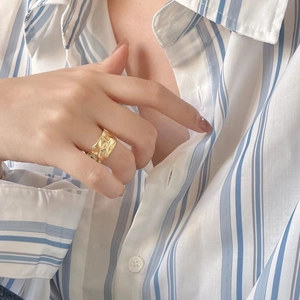 Detailed view of irregular hammered wide gold ring on model wearing striped shirt