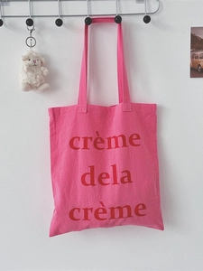 Rosafarbene Canvas-Einkaufstasche mit rotem Aufdruck crème de la crème an weißer Wand