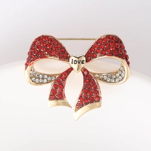 Close-up of golden bow brooch with red crystals and heart engraved with love text