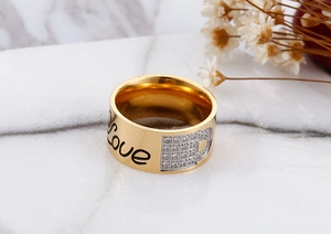 Detail of gold-plated wide band ring featuring Love engraving and cubic zirconia stones