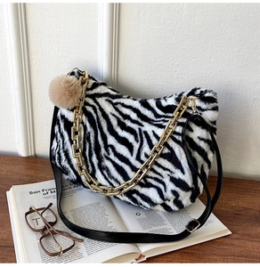 Detail of zebra pattern plush tote with golden chain and fuzzy ball charm on table