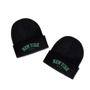 Two black knitted beanies with green NEW YORK USA varsity lettering on plain background