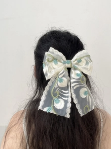 Detail of white lace bow hair clip with green floral embroidery and long mesh ribbons