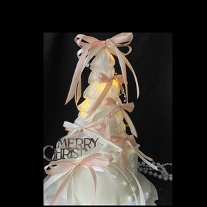 Christmas tree cake decor with pink bows, pearls, and glowing lights on black background