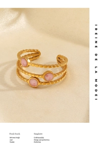 Close-up of a three-layer gold ring with pink stones on a beige textured surface
