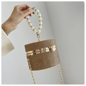 Detail of a golden cylinder evening bag featuring sparkling rhinestones and a pearl handle