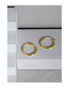 Detailed close-up of chunky gold geometric hoop earrings on a grey stone texture