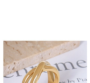 Detailed view of crossover twisted gold ring with a high polished finish on textured background