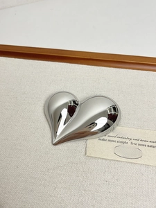 Detailed view of heart-shaped silver brooch with polished finish on textured fabric
