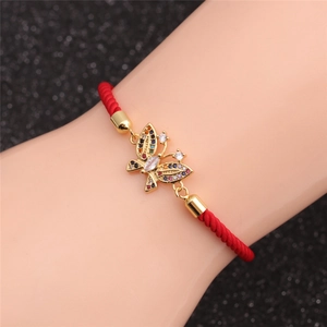 Macro detail of red string bracelet featuring gold butterfly charm with colorful zircon stones