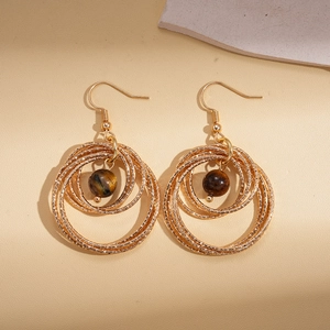 Close-up of layered geometric gold hoops with brown tiger eye beads on stone background