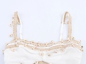 Detail of white bohemian top featuring crochet trim and hanging sea shell decorations