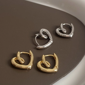 Minimalist twisted heart hoop earrings in gold and silver finish on leather tray