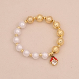 Macro shot of faux pearl bracelet with golden beads and a red ladybug charm with zircon