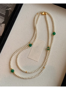 Close-up of double-layered pearl necklace with green beads and gold accents on fabric