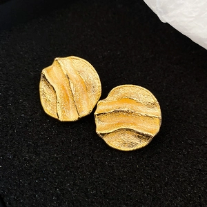 Vue macro de boucles d'oreilles dorées avec texture ondulée et détails métalliques plissés