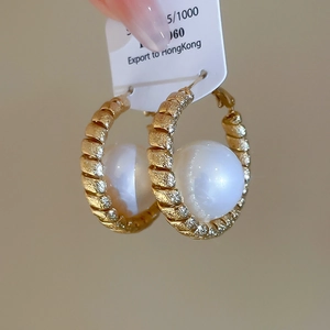 Detail of gold braided hoop earrings with a large white pearl center for a vintage look