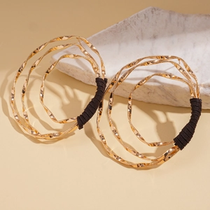 Detail of layered gold geometric twist earrings with dark wrapped wire on a stone base