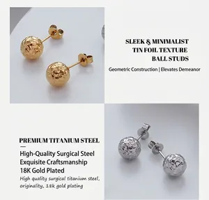 Détail de boucles d'oreilles boules en or et acier avec une texture de surface froissée