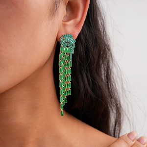 Detail of long emerald green tassel earrings on a model showing golden metal craft