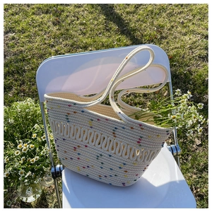 Detail of hand-woven beige tote bag with colorful dots on a white chair in a garden
