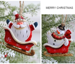 Detail of Santa and Snowman resin ornaments on red sledges hanging on a Christmas tree branch