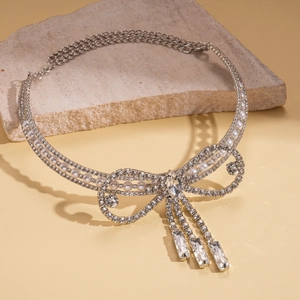 Elegant silver choker necklace with rhinestone bow, pearl tassel on stone surface