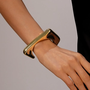 Polished gold geometric triangular open cuff bracelet shown on wrist with black sleeve
