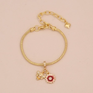 Détail d'un bracelet maille serpent dorée avec breloques abeille, fleurs et cœur