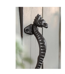 Detail of vintage black cast iron seahorse handle with rustic texture on grey wood door