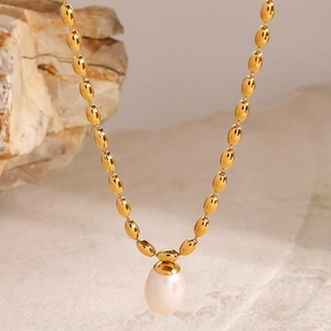 Détail macro d'un collier à billes dorées avec un pendentif perle blanche sur fond de pierre