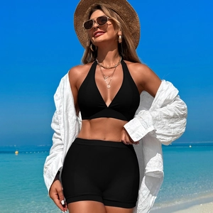 Détail d'un bikini noir dos nu avec une chemise de plage blanche sur le sable