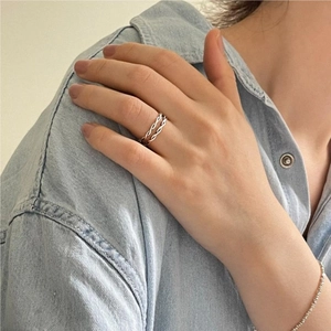 Macro detail of double-layered twisted silver rings on model's hand with denim backdrop