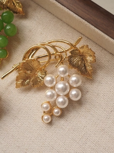 Close-up of a designer grape brooch featuring white pearls and golden metal leaf detail