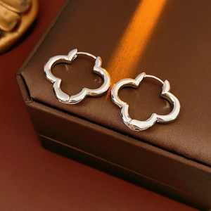 Detailed view of polished silver clover hoop earrings on a textured leather box