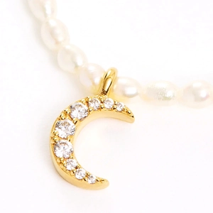 Macro shot of silver crescent moon pendant with round gems on white pearl necklace