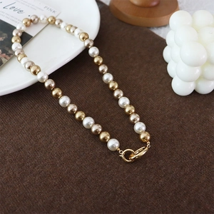 Elegant multi-color pearl necklace with large gold ring clasp on brown knit texture