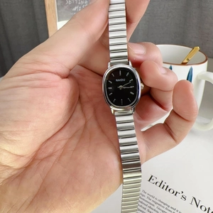 Detail of silver stretch band watch with a black oval dial held in a lifestyle setting