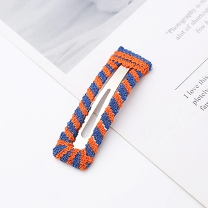 Handmade crochet hair clip with orange and blue stripes on a silver metal base