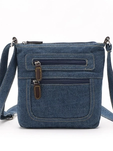 Dark blue denim crossbody bag with multiple zippers and brown leather pulls in front view