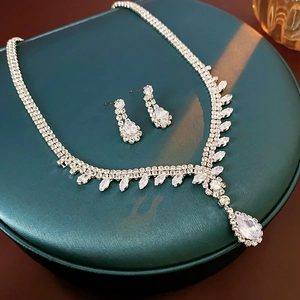 Close-up of sparkling zircon teardrop necklace and earring set on a green display base