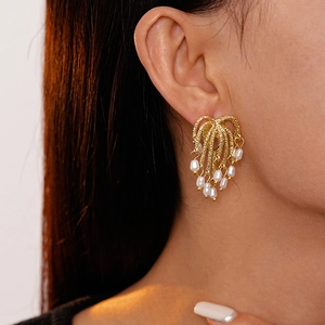 Close-up of gold fringe earrings with imitation pearls worn on model for a luxury look